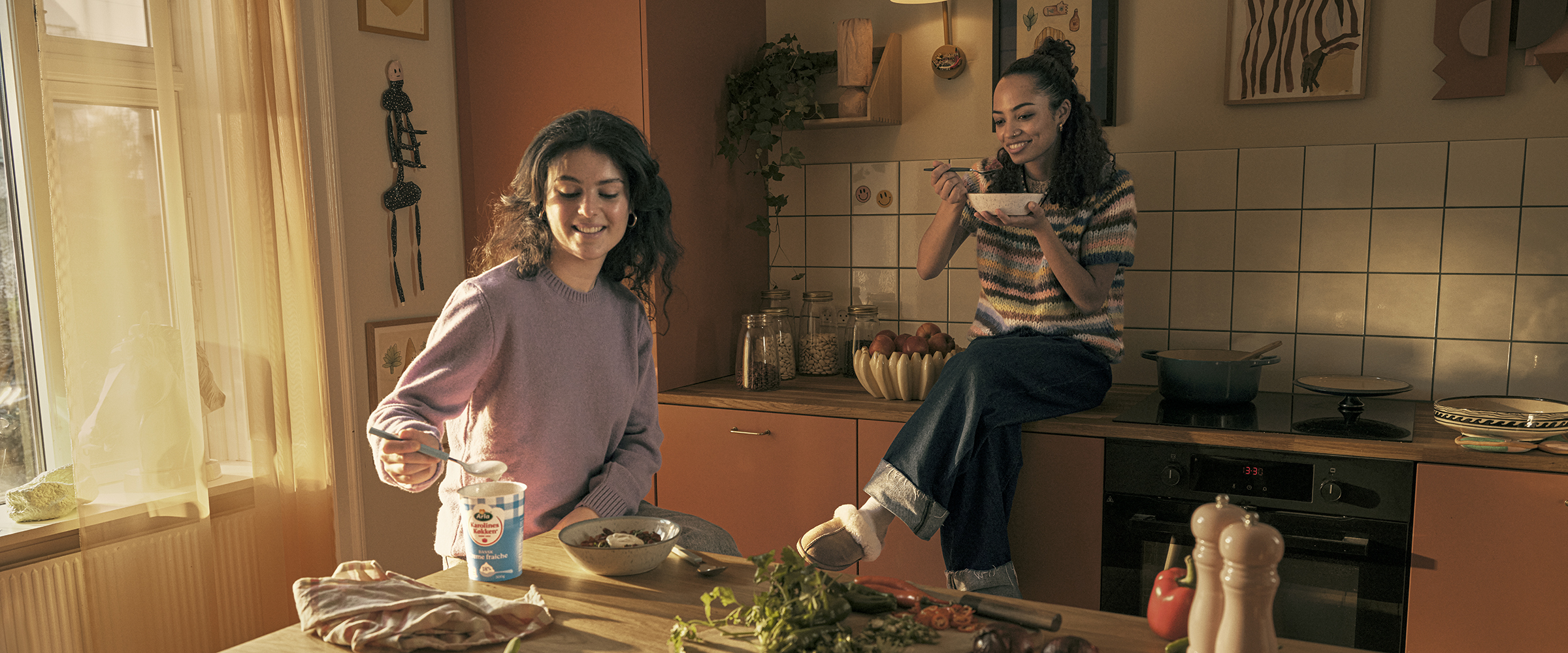 To piger i et køkken spiser mad med creme fraiche